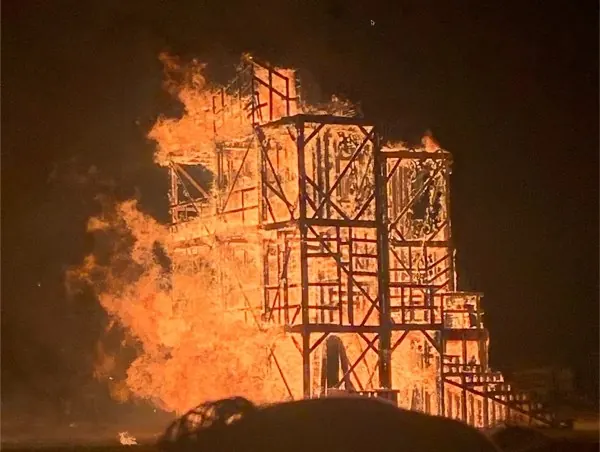 A tall wooden effigy engulfed in flames at night at Burning Flipside 2024